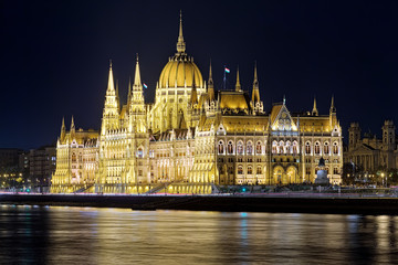 Night view of the Hungarian Parliament Building in bright yellow illumination. View from the bank of Danube in Budapest, Hungary.