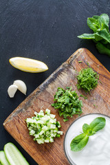 Preparing tzatziki sauce and ingredients, dark stone background