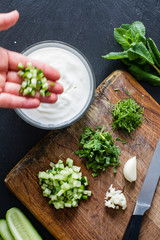 Preparing tzatziki sauce and ingredients, dark stone background