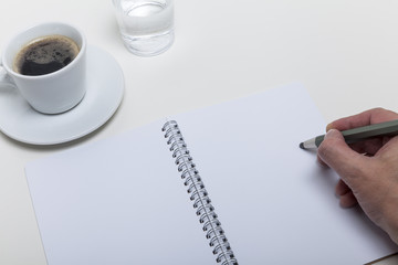 Jemand schreibt etwas mit Bleistift in ein Notizheft, das auf de