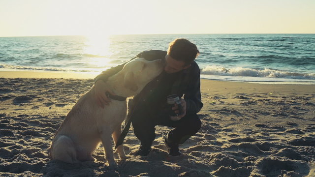 young man with his dog on a beach drinking from thermocup slow motion