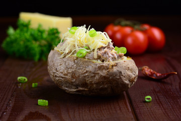 Baked potato stuffed with tuna and cheese garnished with green onion on dark brown wooden table. Low key photography