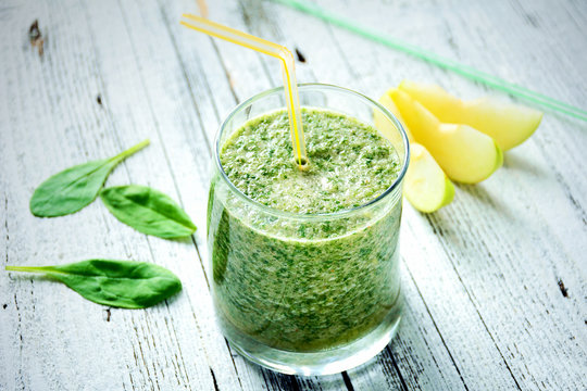 Healthy natural green smoothie with spinach, lemon, green apple and honey in glass with yellow cocktail tube on wooden table