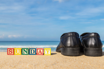 word SUNDAY in colorful alphabet blocks and black shoe on tropic