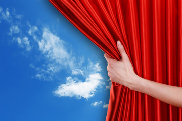 Human hand opens red curtain on sky background
