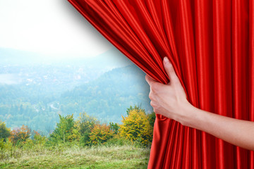 Human hand opens red curtain on nature background
