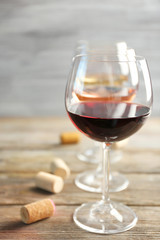 Wine glasses in a row and corks on wooden table against grey background