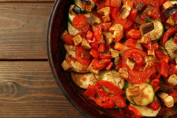 Tasty vegetarian ratatouille made of eggplants, squash, tomatoes and onions in black cast iron pan, on wooden table background