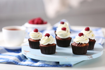 Beautiful chocolate cupcakes with cream and raspberry on table
