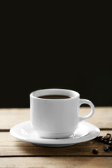 Cup of coffee and coffee grains on wooden table, on gray background