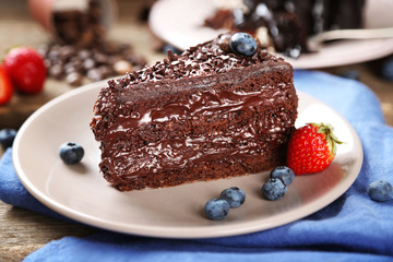 Chocolate cake with cream and fresh berries on plate, on wooden background
