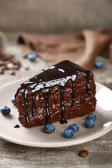 Chocolate cake with chocolate cream and fresh blueberries on plate, on wooden background