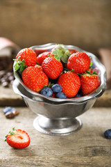 Ripe sweet different berries in bowl, on old wooden table