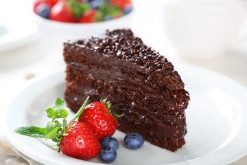 Chocolate cake with chocolate cream and fresh berries on plate, on light background