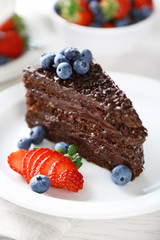 Chocolate cake with chocolate cream and fresh berries on plate, on light background