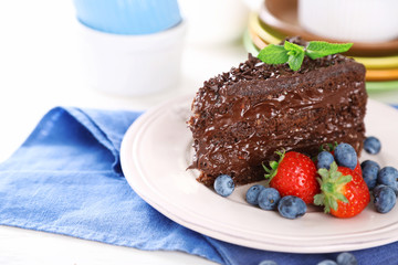 Chocolate cake with chocolate cream and fresh berries on plate, on wooden background