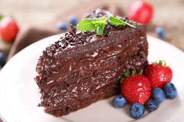 Fototapeta na wymiar Chocolate cake with chocolate cream and fresh berries on plate, on wooden background