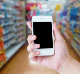 hand holding mobile phone with supermarket shelves aisle blurred