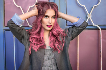 Obraz premium Piękny modniś model z kędzierzawym różowym włosy pozuje przed kolorową ścianą