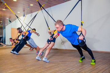 People make fitnes exercise with a band in the gym. TRX