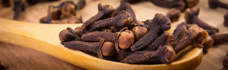 Heap of cloves with wooden spoon on table, seasoning for cooking