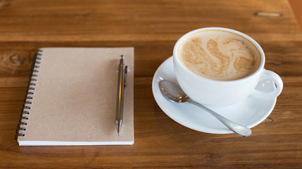 Hot latte art coffee cup on wooden table and note book, vintage