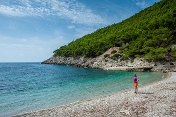 Young woman tourist standing on Mljet beach with turquoise sea water and rocks and pines.