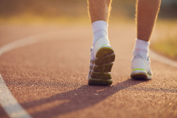 Running sport. Man runner legs and shoes in action on on stadium road outdoors at sunset