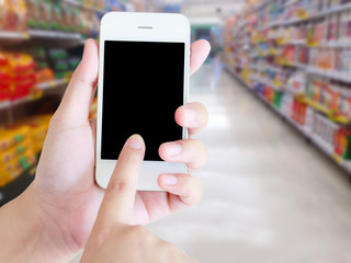 hand holding mobile phone with supermarket shelves aisle blurred