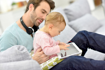 Obraz premium Daddy and baby girl in sofa using tablet and headphones