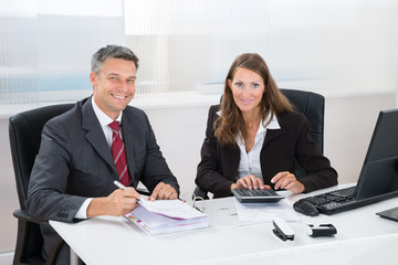 Two Businesspeople Calculating Tax In Office