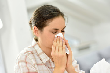 Young woman with cold blowing her nose