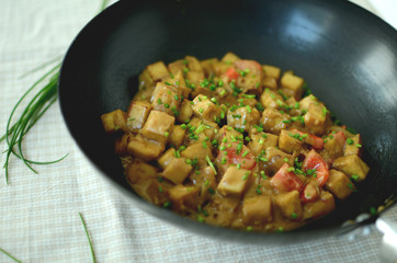 Tofu cubes in a wok skillet with vegetables and creamy sauce