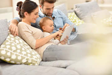 Parents with baby girl in sofa using digital tablet