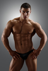 Fototapeta na wymiar Bodybuilder posing. Handsome power athletic male. Fitness muscular body on gray background