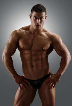 Bodybuilder posing. Handsome power athletic male. Fitness muscular body on gray  background