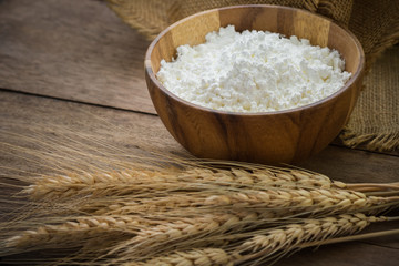 Flour in bowl and wheat on wooden table