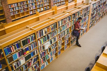 Student reading a book from shelf in library