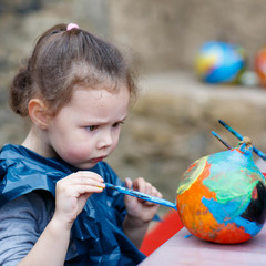 Little kid girl painting with colors on pumpkin