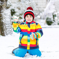 Little boy playing with snow in winter, outdoors.