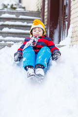 Happy child in colorful clothes having fun with riding on snow,