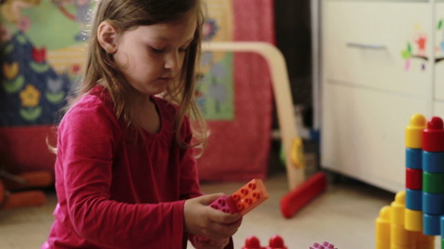 Cute little girl playing with toy blocks at home