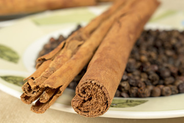 Cinnamon sticks and black pepper grains on decorated dish