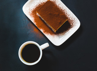 Tasty tiramisu cake with coffee cup on black background
