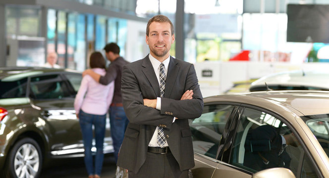 erfolgreicher Gesch&auml;ftsmann im Autohandel - im Hintergrund Kunden & Interieur des Autohauses // 
successful businessman in the car trade - in the background customer & interior of the car dealership