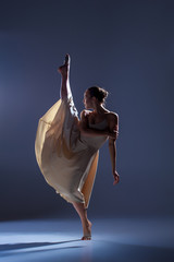 Fototapeta premium Young beautiful dancer in beige dress dancing on gray background
