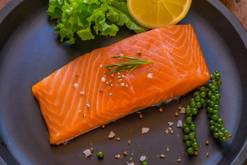 Fresh salmon with lemon on black dish.