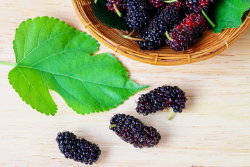 Group of ripe mulberries in wicker basket and putting on wooden
