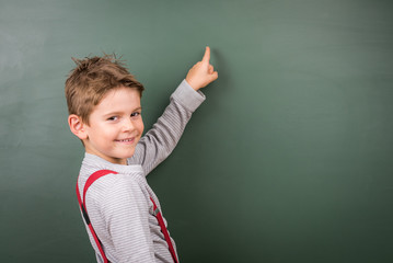 Kleiner netter Junge zeigt auf leere Schultafel