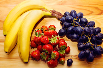 Still life of natural fresh fruit. Bananas, strawberries and blue grapes on the table.